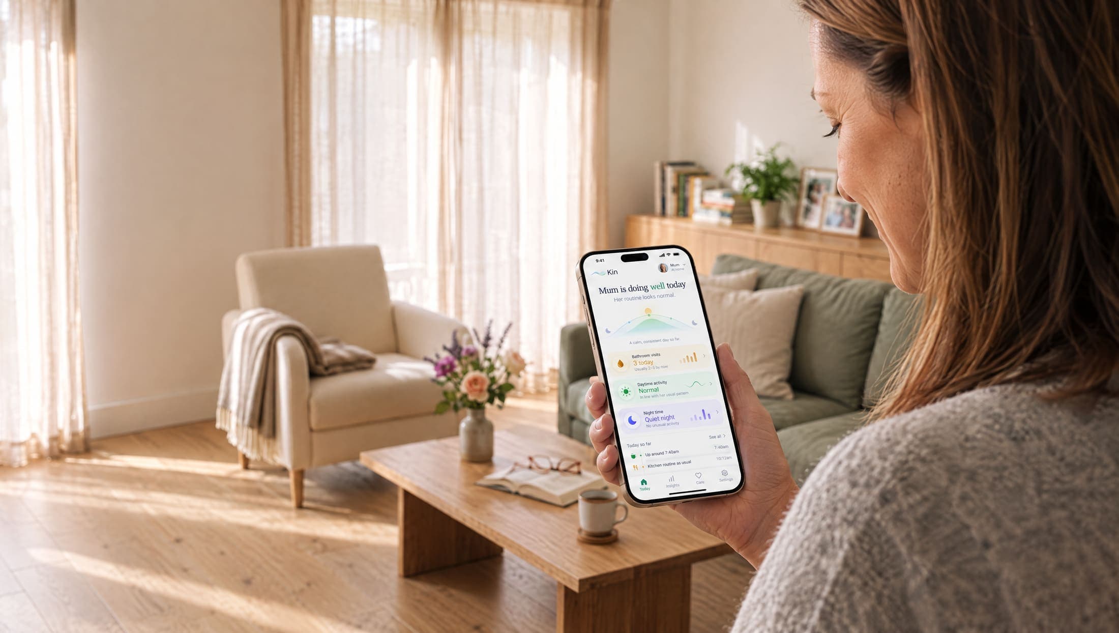 A woman in a sunlit living room looking at the Kin app on her phone